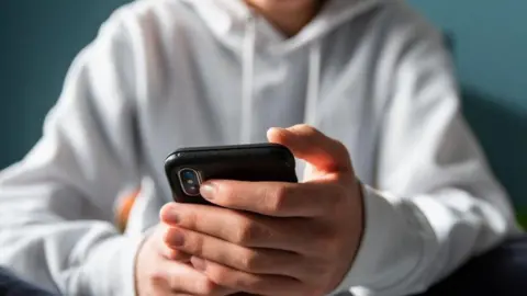 Getty Images A boy, whose face is not visible and is wearing a white shirt, hold a smartphone in his hands