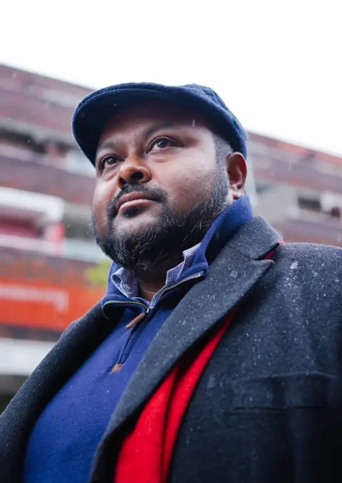 Harry Rose Mish Rahman, wearing a blue jumper and navy blue coat and beret with a red scarf