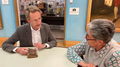 Antiques Roadshow specialist presenter Justin Croft discussing the book with Ms Astin