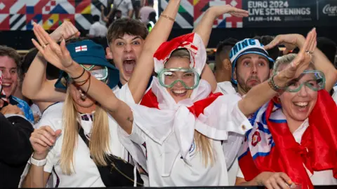 PA Women with England flag tied round her head stretches her arms upwards while wearing green goggles