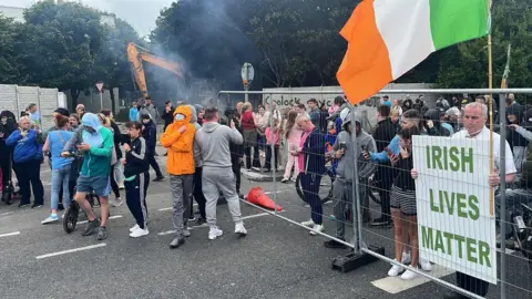 PA Large crowd gathers at barrier in Coolock, including one man holding a sign which reads Irish Lives Matter