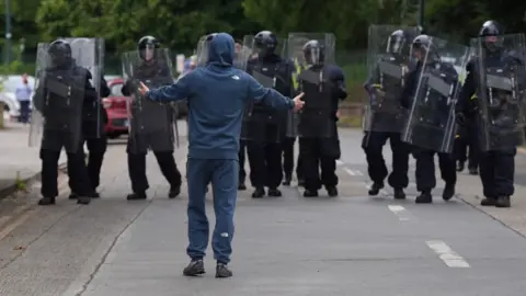 PA Media Man in hooded top with arms outstretched in front of a line of Irish riot police