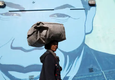 ESA ALEXANDER/REUTERS A woman walks past a mural depicting Nelson Mandela.