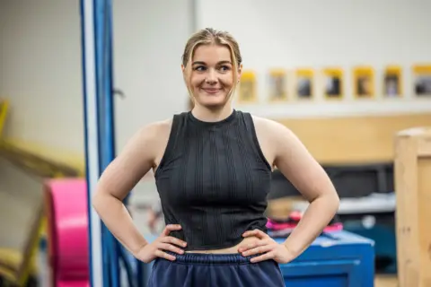 Ellie Kurtzz Meg Hateley in rehearsal wearing a ribbed black vest and navy blue trousers