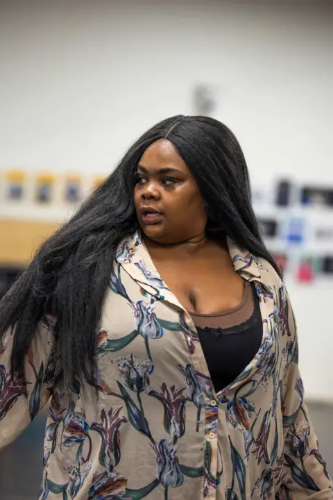 Ellie Kurttz Analisa Lamola in rehearsal wearing a black vest and cream shirt with flowers with her long black hair down