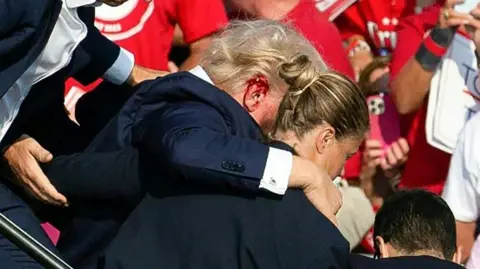 Getty Images Trump, with blood pouring from an ear wound, is hurried off the stage