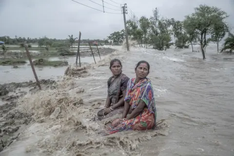 Supratim Bhattacharjee Two women helplessly watch sea waves reclaim their homes in the Sundarbans, India