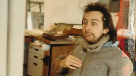 University of Bristol/PA Media Jonny Clothier, pictured in his student days, with long, dark hair, in a room with a cluttered desk