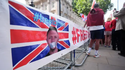 PA Media A campaign banner showing a picture of Tommy Robinson with tape over his mouth