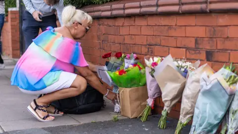 PA Media A person leaves flowers near the scene in Hart Street, Southport, where two children died