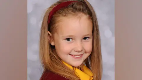 Family photograph  Elsie Dot Stancombe smiles for a photography while wearing a yellow polo shirt and red headband