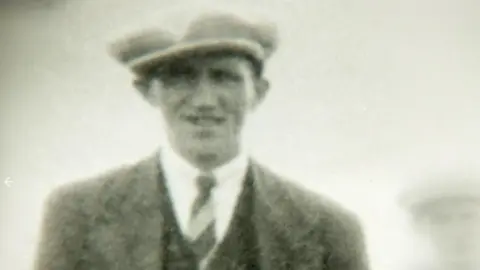 Gleeson Family A black and white image of a young man with a suit, tie and cap on 