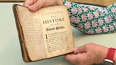 BBC Two hands holding the top and bottom of a visibly worn book. The book is open. The pages are yellow.