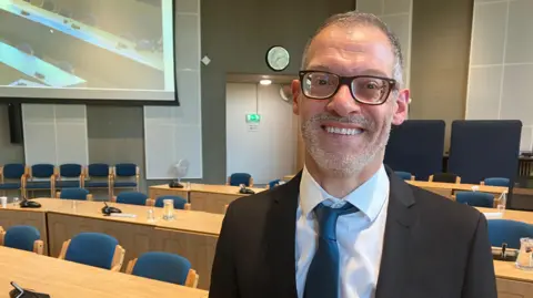 BBC A picture of a council leader Adam Zerny in a black suit with a dark green tie