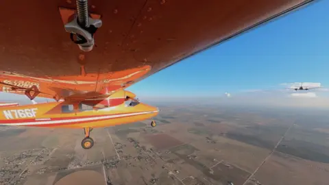 Aerolane An small orange aircraft is flying, towed by another aircraft ahead