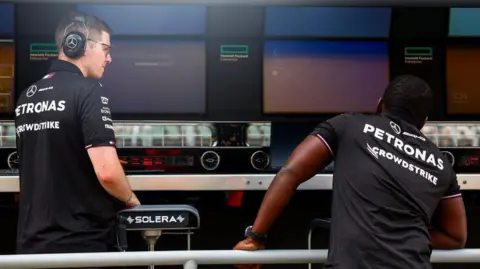 Getty Images A Mercedes team member, whose shirt bears the logo of team sponsor Crowdstrike, looks on as Windows error screens are seen 