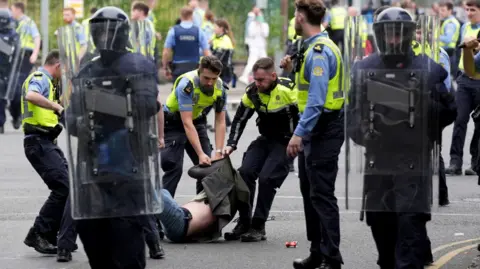 PA Media Man on the ground with coat pulled up over his head is grabbed by Irish police officers