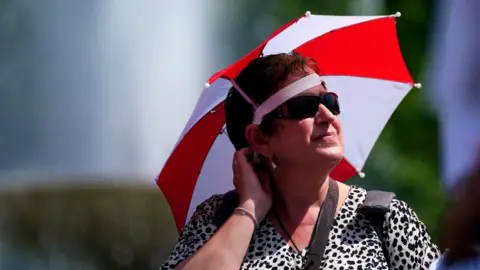 PA Media A woman protects her face from the bright sun with a headshield