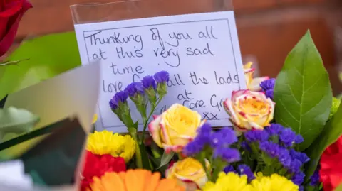 PA Media Purple, yellow and red flowers in a bouquet, with a message, reading: Thinking of you all at this very sad time