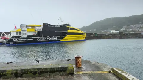 The Atlantic Wolff, a yellow and black ferry, at Newlyn harbour. It is on the water docked on a quay 