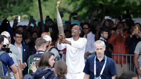 Getty Images US rapper Snoop Dogg holds the torch as part of the 2024 Paris Olympic Games Torch Relay, on the day of the opening ceremony, in Saint-Denis, outside Paris, on July 26, 2024.