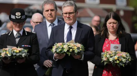 PA Media Merseyside Chief Constable Serena Kennedy, in full uniform, Liverpool City Region Mayor Steve Rotheram, in a grey suit, Prime Minster Sir Keir Starmer, in a black suit, and Merseyside Police and Crime Commissioner Emily Spurrell, in a red and black dress, carry floral wreaths to lay in tribute to those killed in the Southport attack