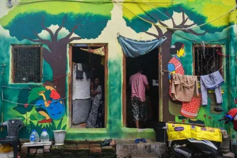 Getty Images A woman is standing inside her colorfully painted house in a slum area in Kolkata, India, on June 23, 2024. 