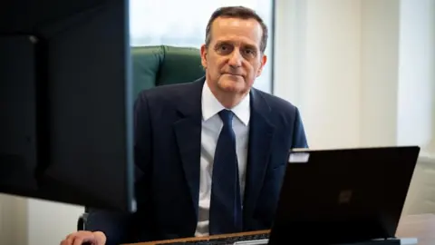 PA Media Stephen Parkinson sits at his desk