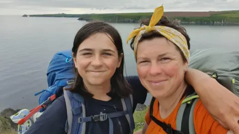 Kerry-Anne Finn and Kerry-Anne on the Wales Coast Path, they are both smiling and looking at the camera. Finn is wearing a blue t-shirt and Kerry-Anne is wearing an orange t-shirt and her hair is tied back in a yellow bandana