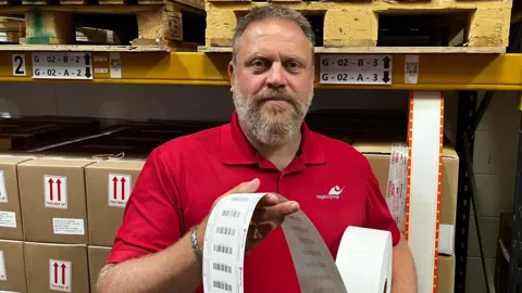 Nagels Lee Minter holding a roll of tickets, standing in front of some boxes