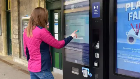 Northern A women in a pink jacket buys a ticket from a Northern ticket machine