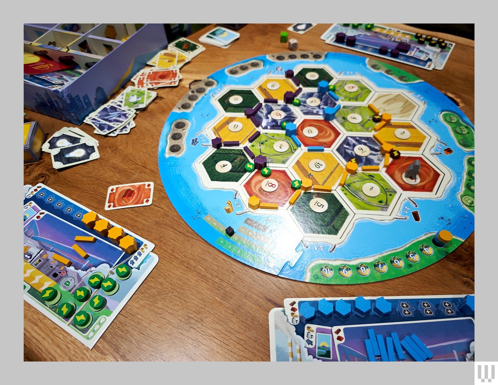 Overhead view of a boardgame set up on a table including a large circular board player cards and stackable pieces