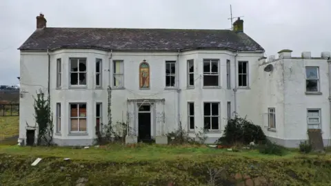 Getty Images Marianvale mother and baby home from the outside. It is white with some windows broken. There is a stained glass window on the front.