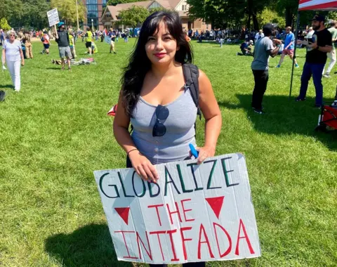 Mike Wendling / BBC A woman holds a sign reading "Globalize the Intifada"