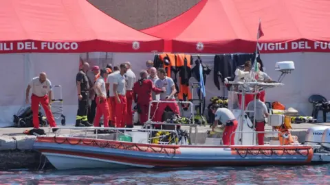 PA Media Group of fire service dive team in uniform next to a rescue boat, with emergency tents in the background