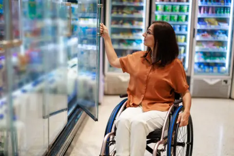 Getty Images A woman in a wheelchair opens a fridge door in a supermarket