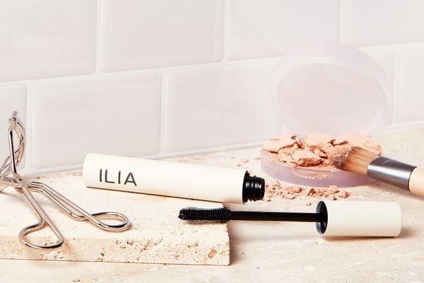 ILIA Limitless Lash Lengthening Clean Mascara displayed on a counter next to an eyelash curler and makeup powder