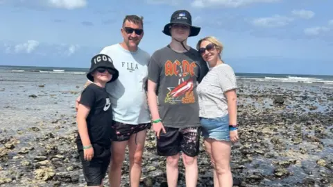 Supplied Hector and his family on holiday. They are standing on a rocky beach with the sea behind them.