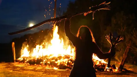 PA Re-enacted scene of a Viking woman holding a stick above her head in front of a firey scene