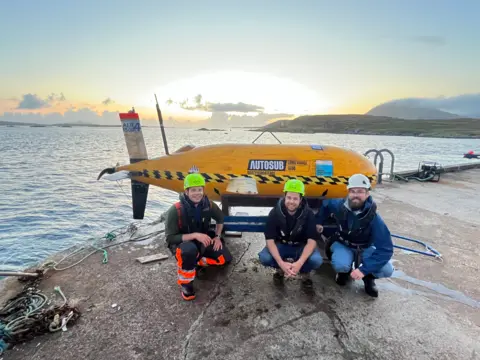 NOC Boaty McBoatface with three engineers on a quayside on Isle of Harris