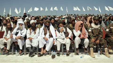 Rolling Narratives  Image from documentary Hollywoodgate, showing the Taliban, sitting in a row, in front of a crowd of people