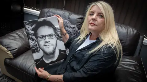 Phil Coomes/BBC Angela Stevens holds a large photo of her son Brett