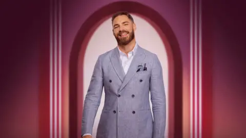 Netflix Publicity shot featuring Steven Smith in a grey jacket and white shirt smiling at the camera, framed by a pink archway