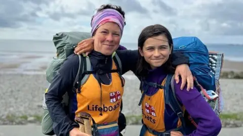 Kerry-Anne Kerry and Finn selfie while walking in Wales, they are smiling at the camera and each have a backpack on and a yellow RNLI lifeboats vest over their tops