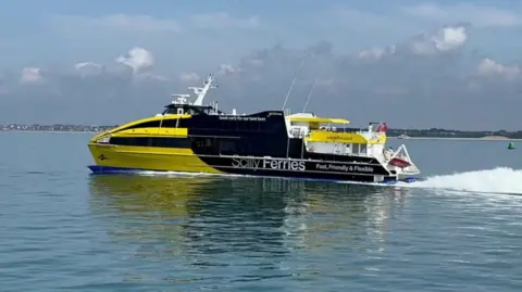 BBC The Atlantic Wolff, a yellow and black ferry, moving over the water to the left of the picture with the white wake visible behind