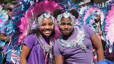 PA Media Two girls in pink and purple outfits pose during the Children's Day Parade