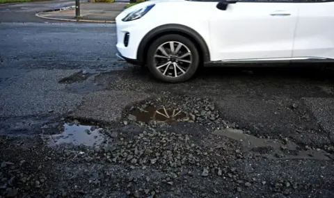 Getty Images A white car driving over several potholes on a road in Britain