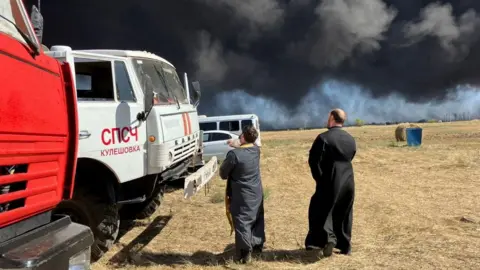 Reuters Russian Orthodox clergymen sprinkle holy water on fire trucks during a service near the scene of a fire at the Proletarsk fuel depot