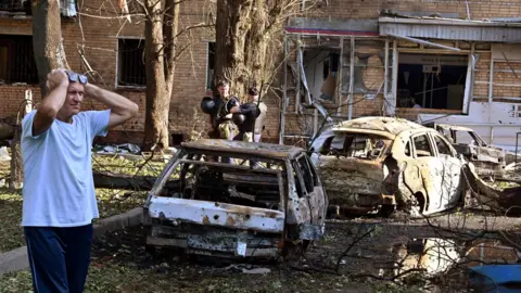 Reuters A man reacts while standing next to burnt-out remains of cars