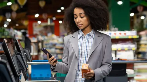 Getty Images Unimpressed woman at self-checkout till paying for item using her phone